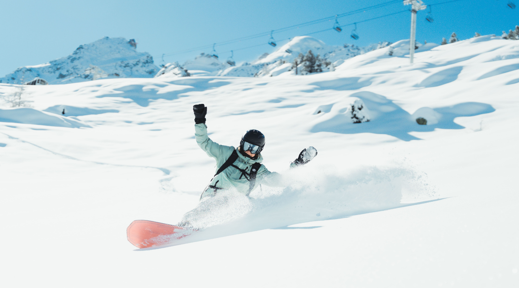 Person snowboarding down a snowy slope with mountains in the background