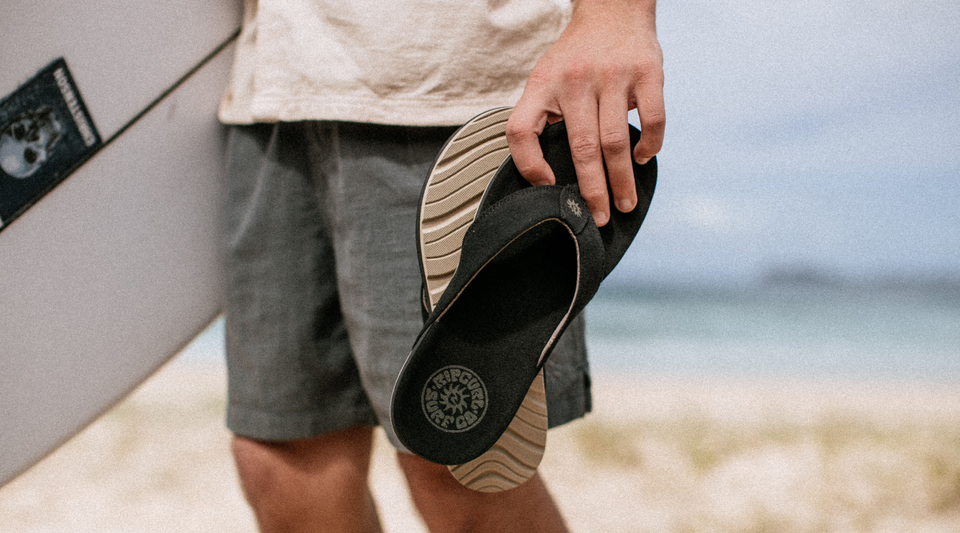 Person holding a sandal on a beach with a blurred background